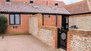 A brick cottage with a tiled roof, a gravel driveway, and a gate with a sign indicating it is for Hitchens Cottage. - Hitchens Cottage (Norwich)