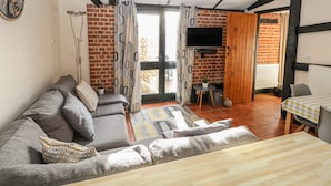 A cozy living room with a sofa, a wooden table, and a TV mounted on a brick wall. - Hitchens Cottage (Norwich)