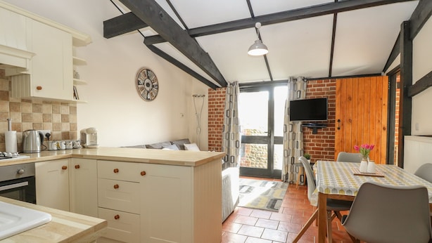 A kitchen with a central island, a dining area with a table and chairs, and a brick wall. - Hitchens Cottage (Norwich)
