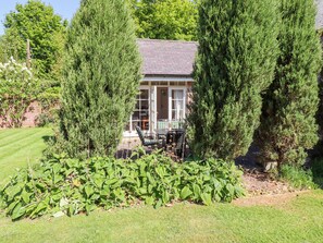 A house with a patio area, surrounded by tall evergreen trees, and a well-maintained lawn. - The Coach House (Berwick-upon-Tweed)
