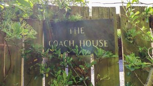 Un letrero con el texto “THE COACH HOUSE” rodeado de follaje.