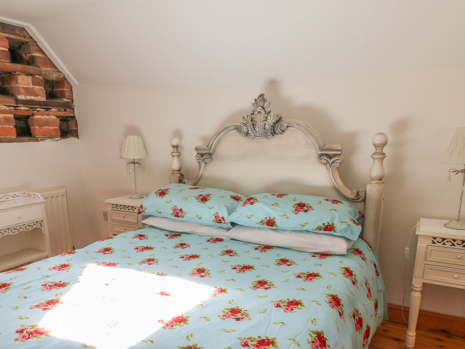 Un dormitorio con una cama, dos mesitas de noche, una lámpara y una pared de ladrillo.