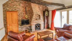 A cozy living room with a brick fireplace, leather sofas, a wooden coffee table, and a television. - Forge Cottage (Gainsborough)