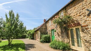 A stone house with a paved driveway, a green door, and a window with a shutter. - Forge Cottage (Gainsborough)