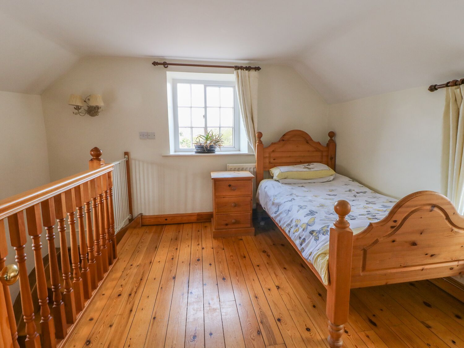 A bedroom with a wooden bed, a nightstand, a dresser, a window with curtains, and a radiator.