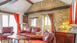 A cozy living room with leather furniture, a stone wall, and a wooden ceiling. - Forge Cottage (Gainsborough)