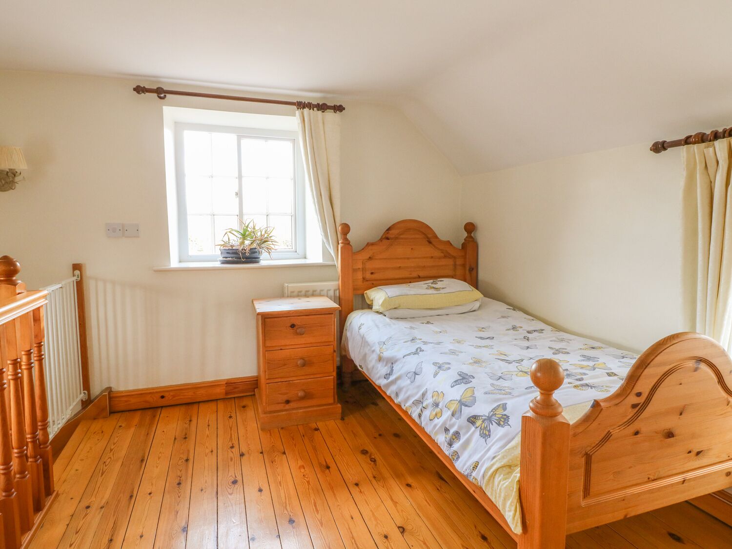 Quarto com cama de madeira, mesa de cabeceira, cómoda, janela com cortinas e radiador.