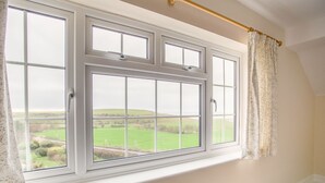 A room with a large window overlooking a green landscape, a curtain rod, and a green wall. - The Doves (Bridport)