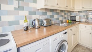 A modern kitchen with a washing machine, a toaster, and a kettle on the counter. - The Doves (Bridport)
