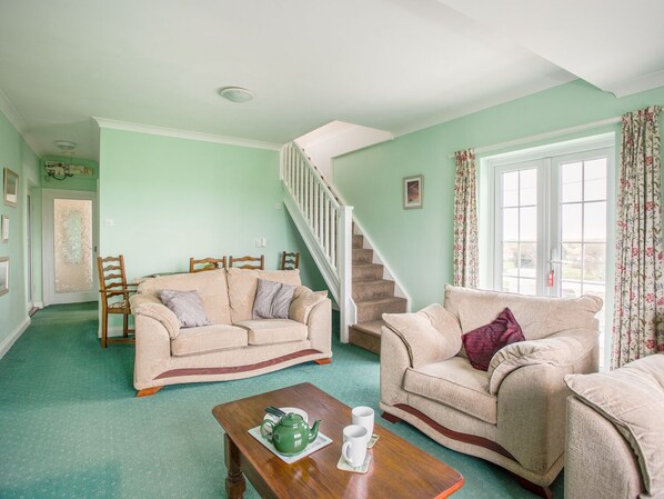 Una sala de estar con alfombra verde, dos sofás color beige, una mesa de centro de madera y una escalera.
