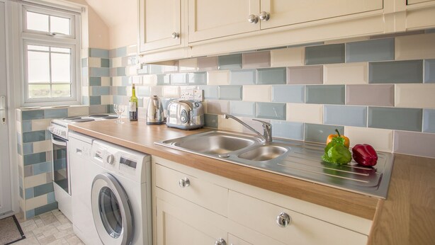 A compact kitchen with a washing machine, a toaster, and a sink. - The Doves (Bridport)