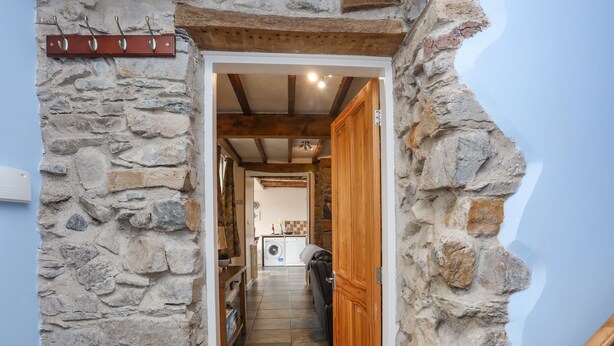 A stone-walled hallway leading to a kitchen with a washing machine and a wooden door. - Plas Cefn Mawr (Llanfairpwllgwyngyll)