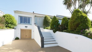A modern two-story house with a white exterior, a wooden garage door, and a staircase leading to the entrance. - Keelyn (Newquay)