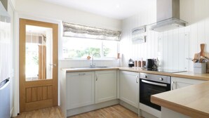 A kitchen with white cabinets, a wooden countertop, a stove, and a window with a view of greenery outside. - Keelyn (Newquay)