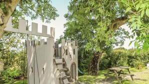 Un espace de jeux sur le thème du château, avec une balançoire, un toboggan et une table de pique-nique.