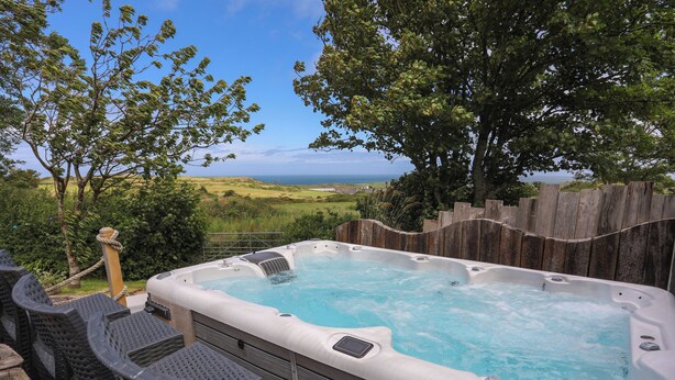 Un bain à remous avec vue sur l’océan, entouré d’une clôture en bois et de verdure.