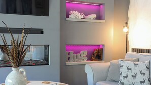 Un salon moderne avec un canapé, une table basse agrémentée d’un vase décoratif et deux étagères éclairées, sur lesquelles sont disposés des objets décoratifs.