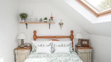 A bedroom with a sloped ceiling, a wooden bed frame, a green leaf-patterned bedspread, bedside tables with lamps, and a skylight.