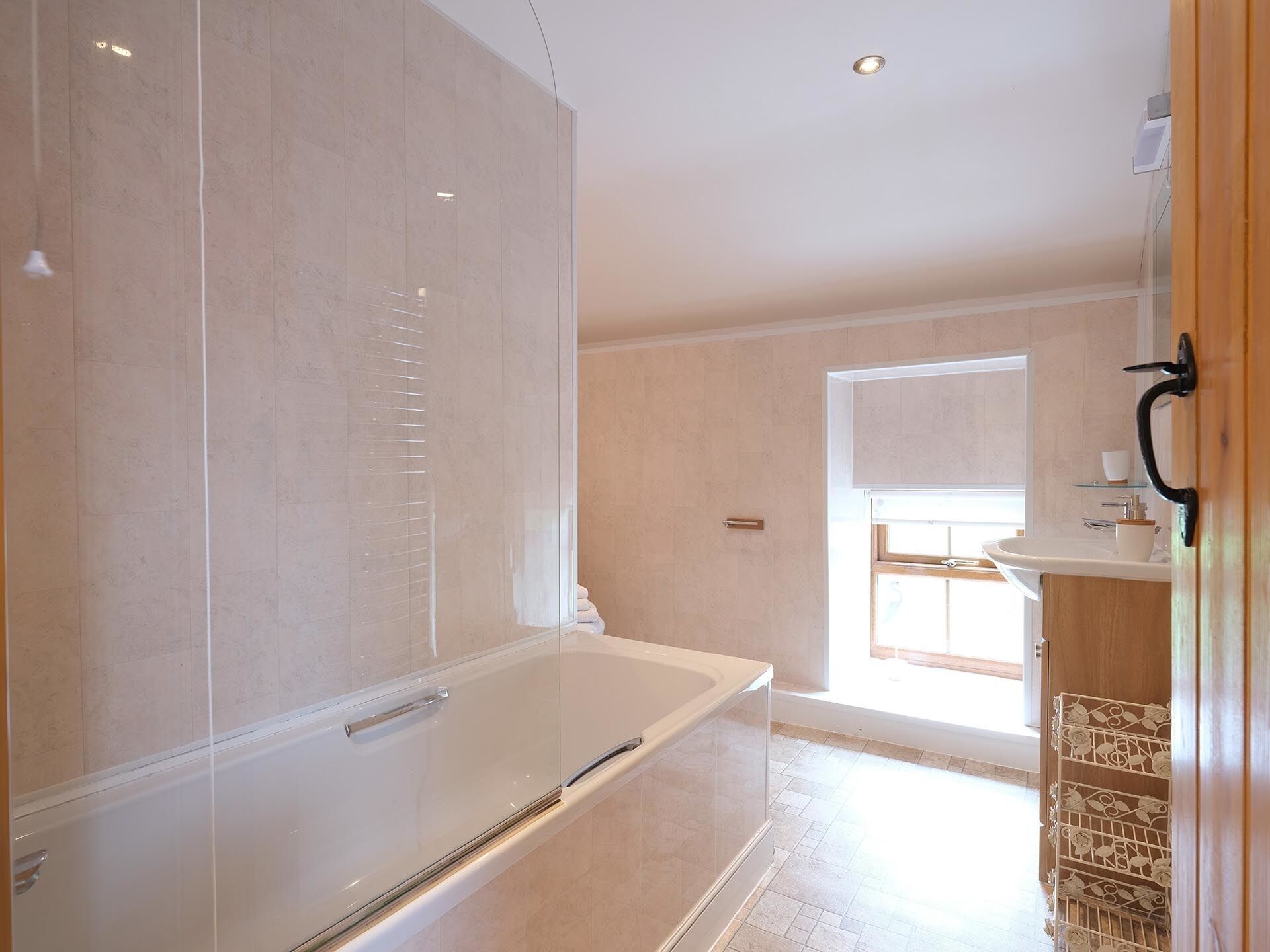 Een moderne badkamer met een douchecabine van glas, een wit bad en een houten wastafelmeubel met een wastafel.