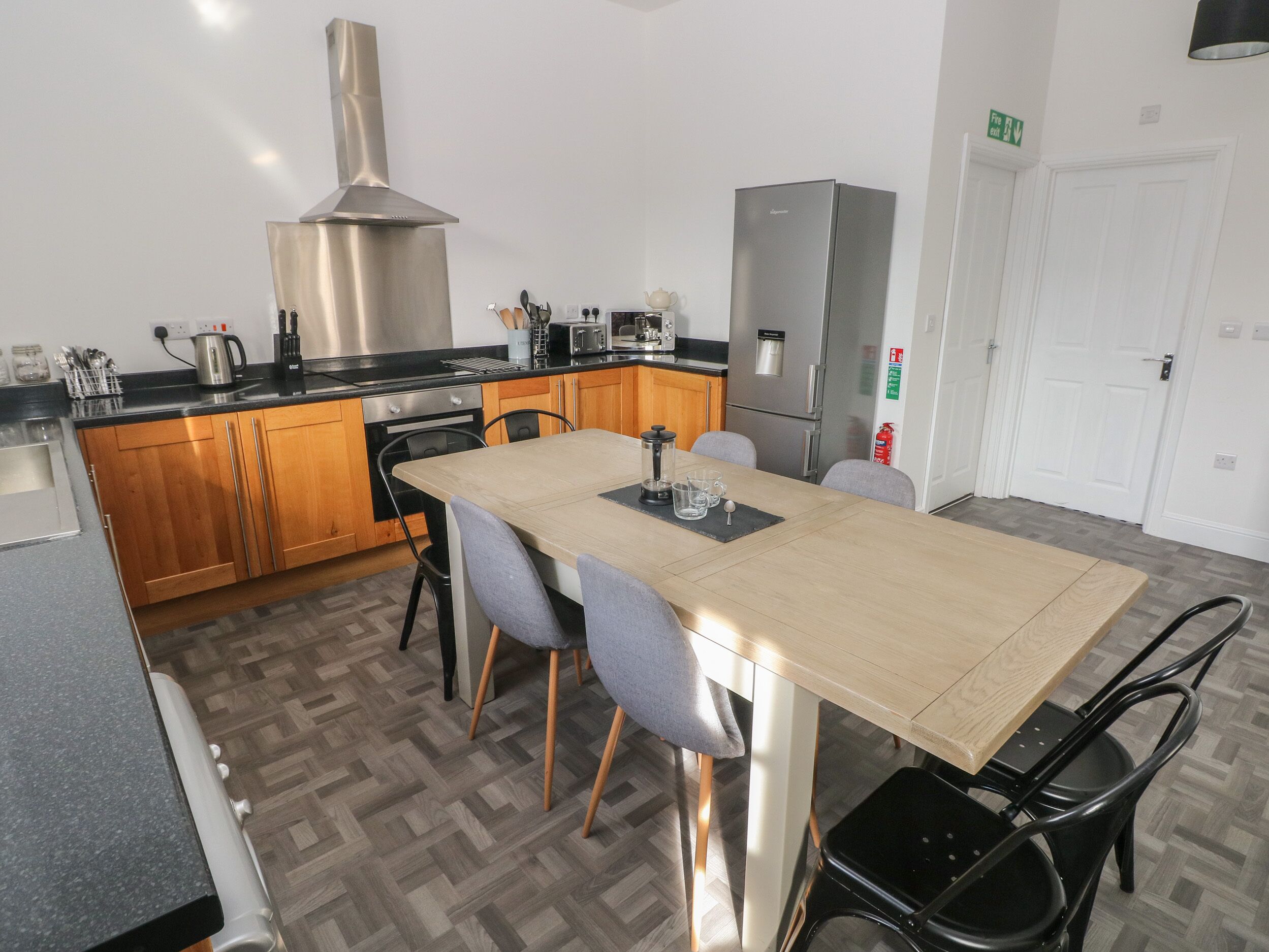 A modern kitchen with wooden cabinets, a stainless steel range hood, a refrigerator, and a dining area with a table and chairs.