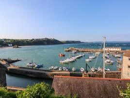 A harbor with numerous boats docked, a stone wall, and a building with a red roof.