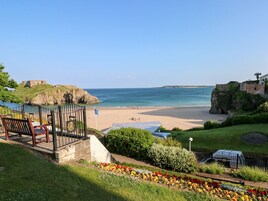 A coastal view with a beach, a historic fort, and a gazebo with benches.