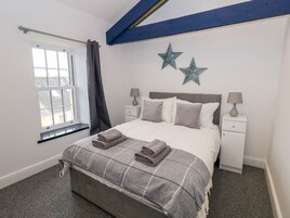 Un dormitorio con una cama, dos mesitas de noche, un ventanal con cortinas y dos adornos con forma de estrella en la pared.