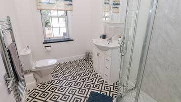 A bathroom with a geometric patterned floor, a toilet, a sink, a cabinet, a window with a view, and a shower area.