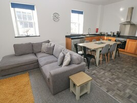 A modern kitchen with a dining area, a grey sofa, and a small wooden stool.