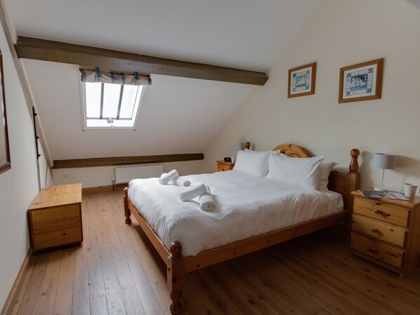 A bedroom with a wooden bed, a nightstand, a dresser, a window with a view, and two framed pictures on the wall.