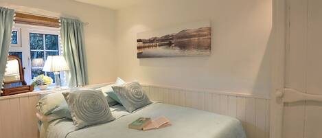 A bedroom with a bed, a window with curtains, a lamp, a painting on the wall, and a wardrobe.