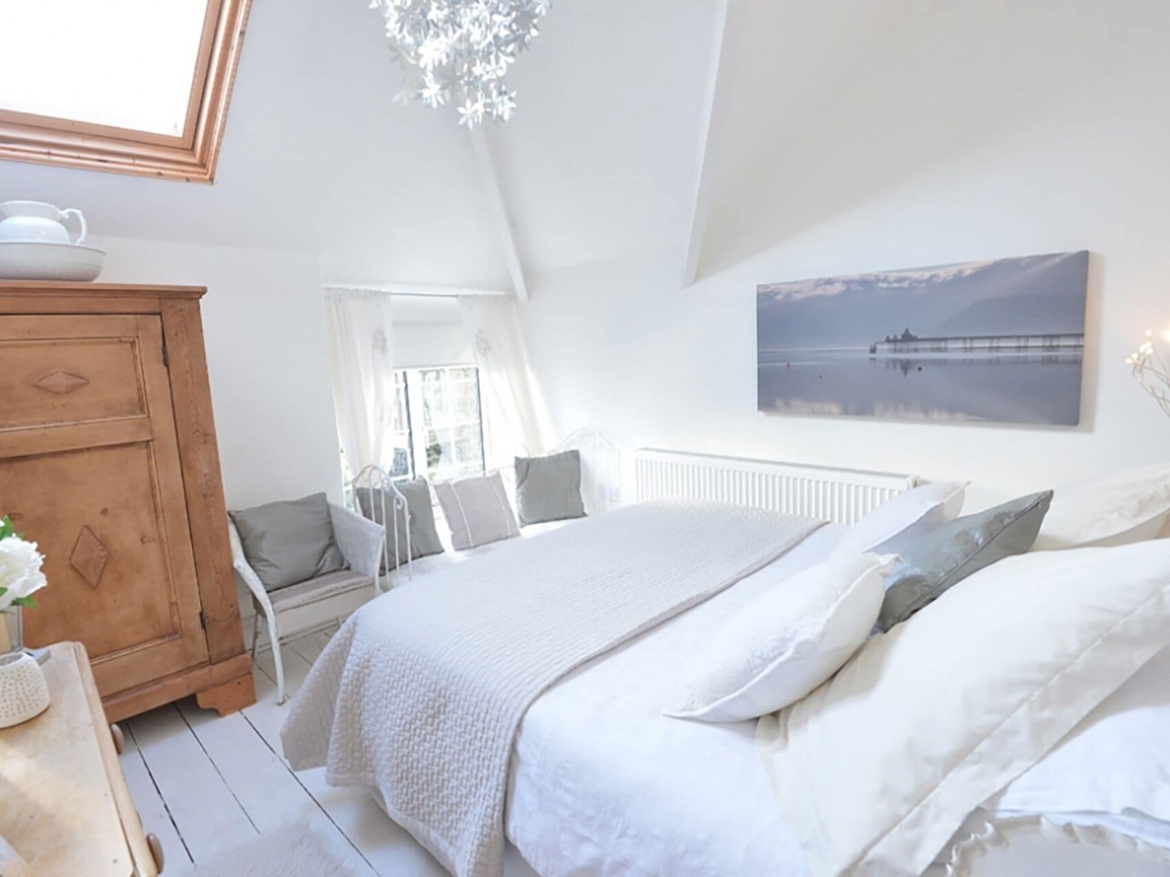 Une chambre à coucher avec un lit, une commode en bois, une fenêtre avec des rideaux et un tableau accroché au mur.