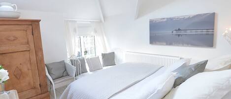 Une chambre à coucher avec un lit, une commode en bois, une fenêtre avec des rideaux et un tableau accroché au mur.