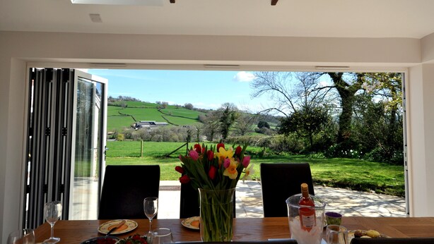 A dining table with a vase of flowers, a bottle of wine, and a glass of water. - Culverwells (Axminster)