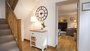 A staircase with wooden railings leading to a living area with a fireplace, a clock, and a white cabinet with baskets.