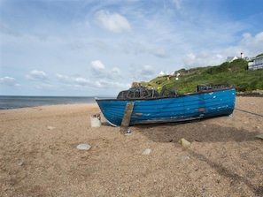 A blue boat on a sandy beach with a clear sky and distant buildings.