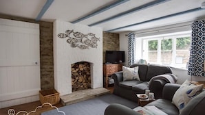 Ein gemütliches Wohnzimmer mit Kamin, einer Couch, einem Fernseher und einem Fenster mit gemusterten Vorhängen.