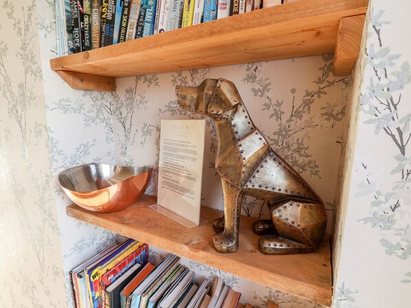 Una estantería de madera con libros, una escultura de metal y un cuenco metálico.