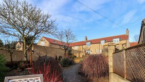 A brick pathway leading to a row of stone houses with red roofs. - The Pheasantry (Scarborough)