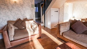 A cozy living room with two leather sofas, wooden flooring, and floral wallpaper. - The Pheasantry (Scarborough)
