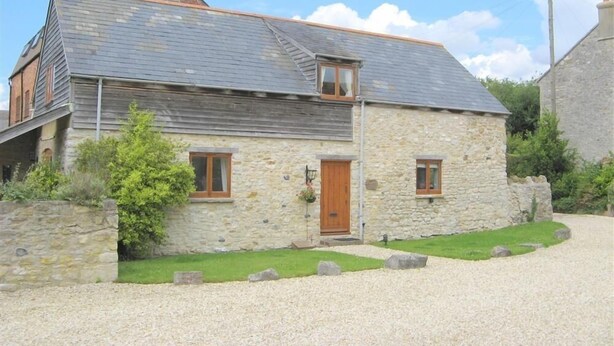 Une maison en pierre avec un toit en pente, une porte en bois et une allée gravillonnée.