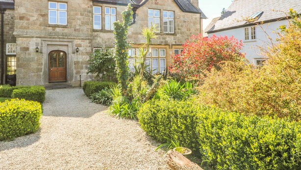 A stone building with a traditional design, featuring a gravel driveway and well-maintained gardens. - Surf Song (Penzance)