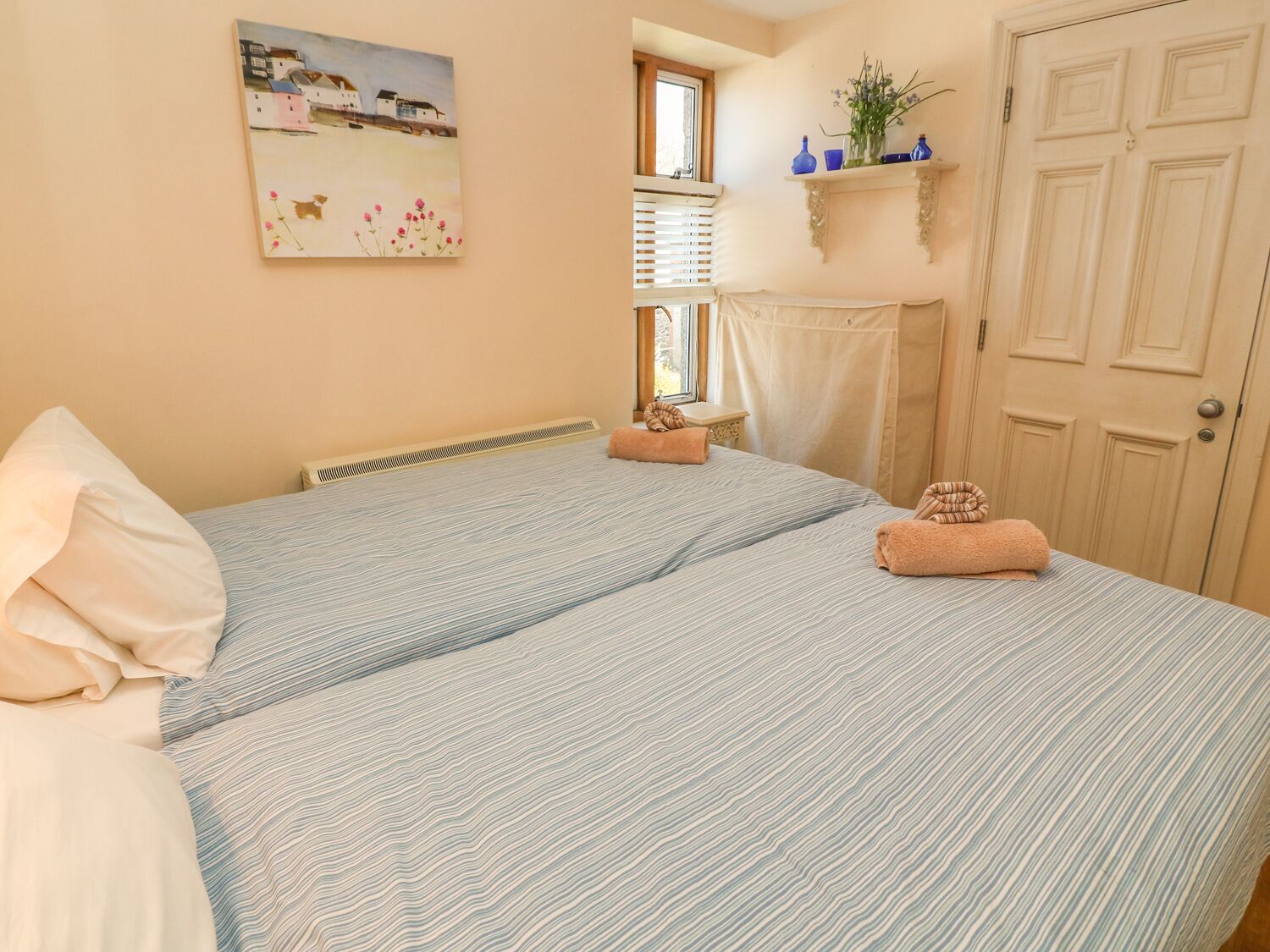 A bedroom with a bed, a window, a door, and a painting on the wall.
