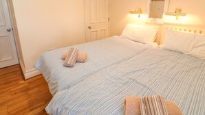 A double bed with striped bedding, a white door, and a wall-mounted mirror with lights. - Surf Song (Penzance)