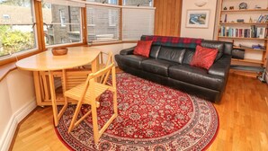 A cozy living room with a black leather sofa, a wooden coffee table, and a red patterned rug. - Surf Song (Penzance)