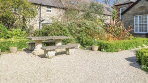 A stone building with a gravel courtyard, a stone bench, and various plants. - Surf Song (Penzance)