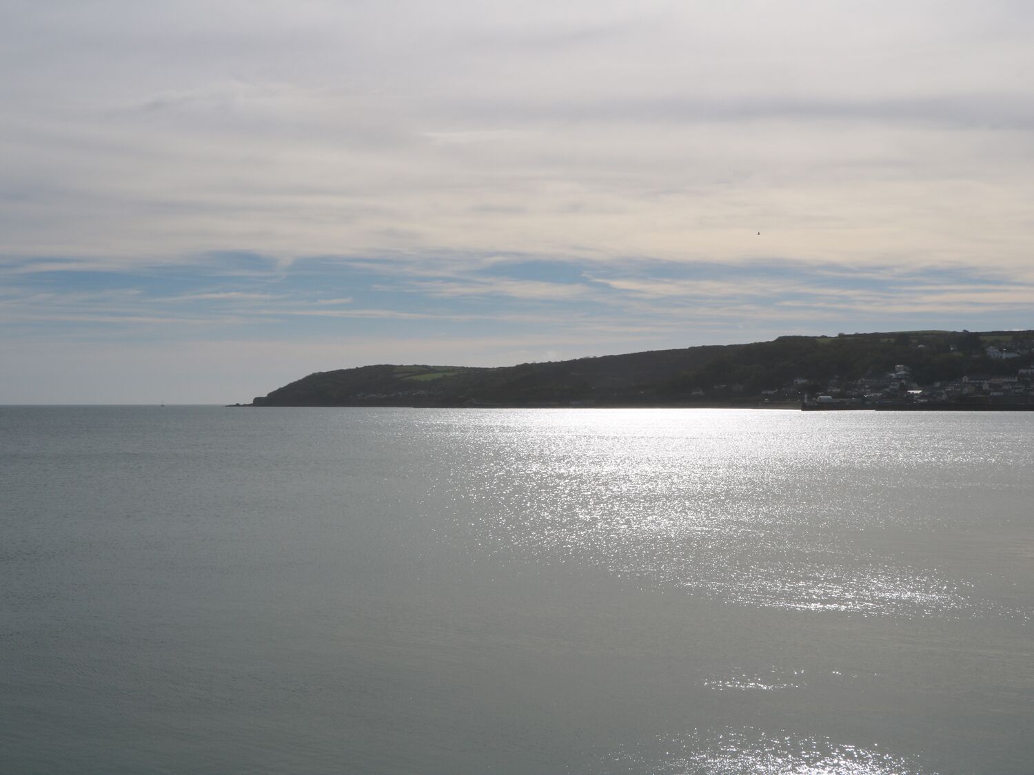 A coastal view with a calm sea, a distant landmass with buildings, and a clear sky.