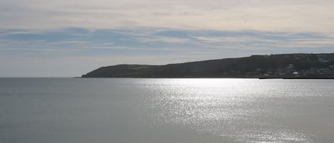 A coastal view with a calm sea, a distant landmass with buildings, and a clear sky.