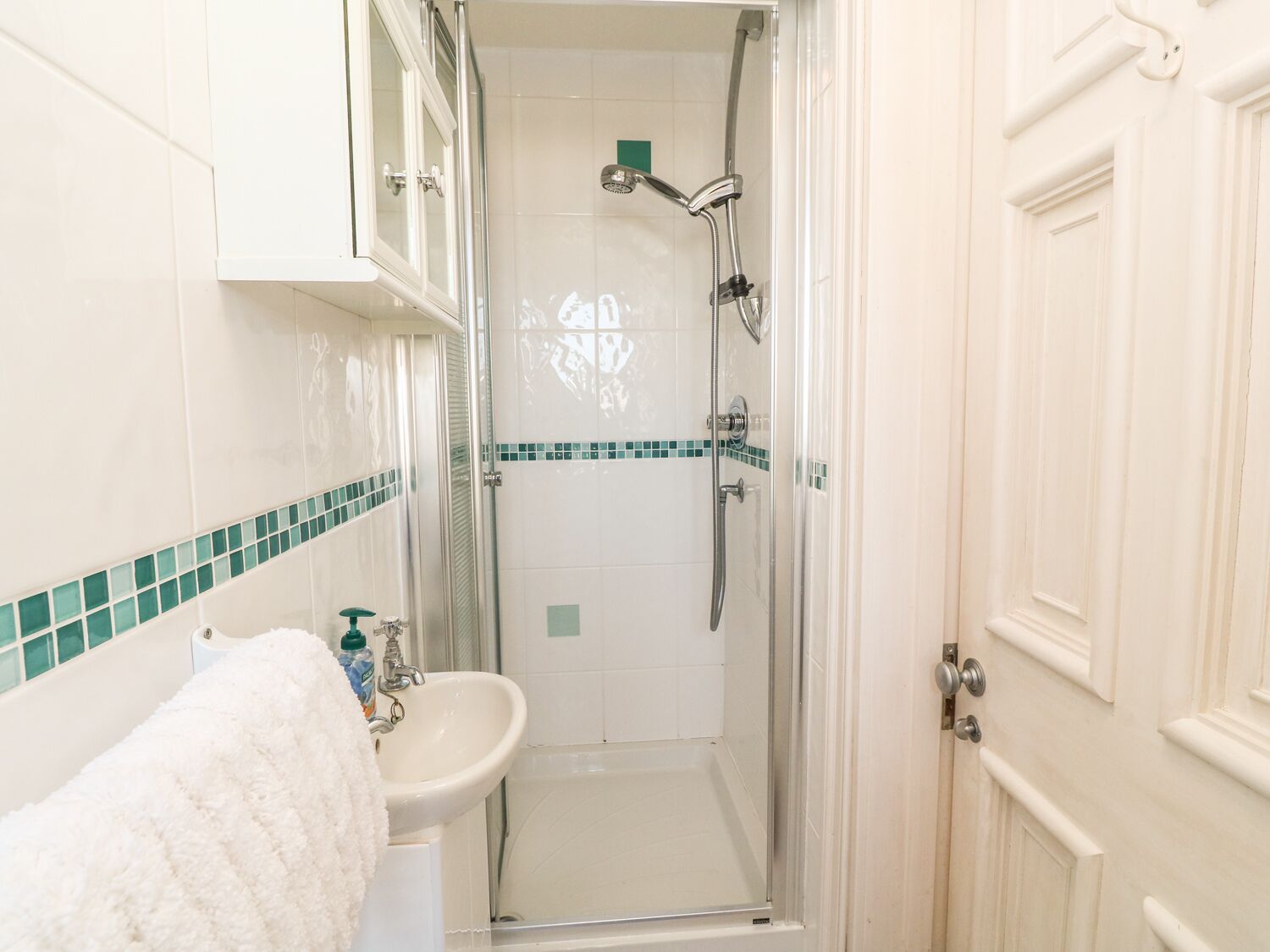 Un baño con cabina de ducha de vidrio, un lavamanos y una toalla blanca.