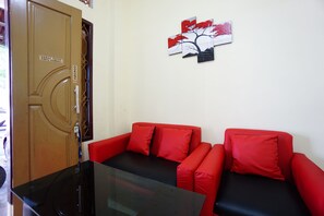 A room with a red sofa, a black glass table, and a wooden door with a sign. - OYO 1912 Kengkang Residence (Manado)